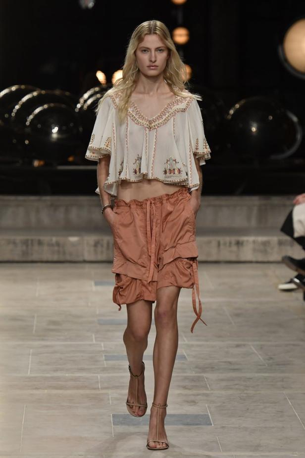 Eine blonde Frau in einem bauchfreien Oberteil und Shorts auf einem Laufsteg.