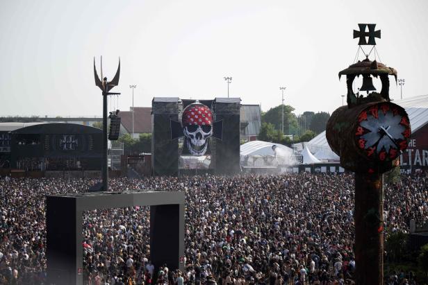 Eine große Menschenmenge vor einer Bühne mit einem Totenkopf-Banner bei einem Musikfestival.