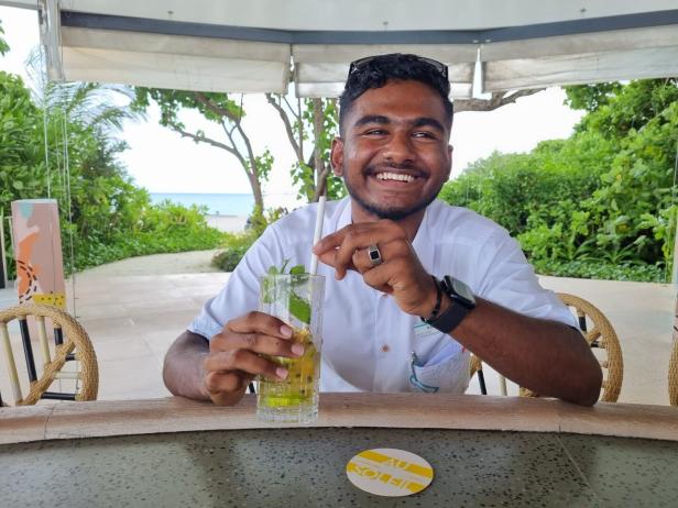 Mitarbeiter im Hotel auf den Malediven in einer Strandbar, trinkt einen alkoholfreien Maracuja Cocktail und lächelt