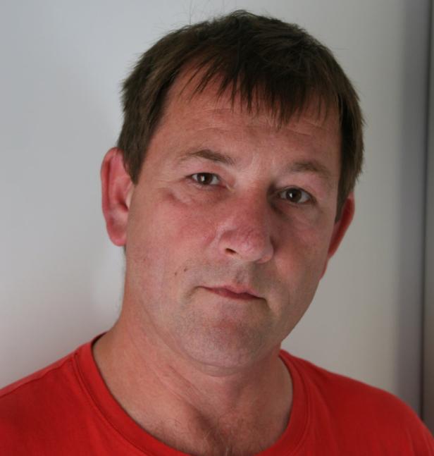 Ein Mann mit braunen Haaren und einem roten T-Shirt blickt in die Kamera.