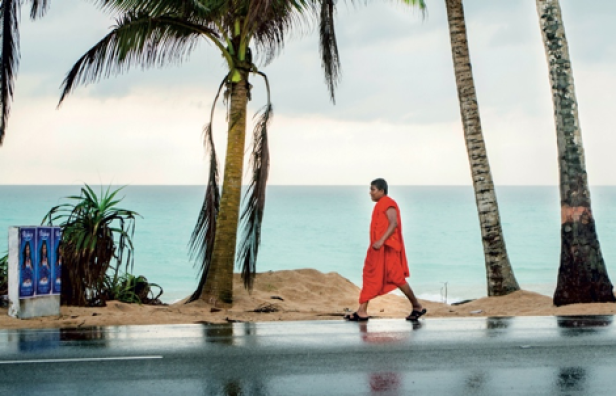 Ein buddhistischer Mönch geht an einem Strand mit Palmen entlang.