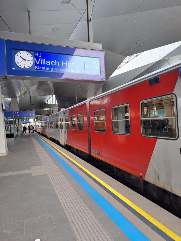 Eine S-Bahn-Garnitur an einem Bahnsteig an dem ein Railjet nach Villach angezeigt wird