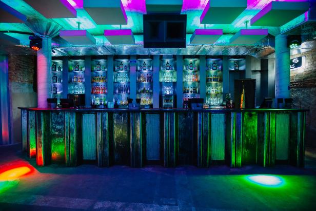 Eine Bar mit bunten Lichtern und Spirituosen im Regal.
