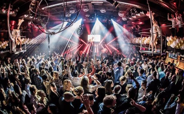 Eine große Menschenmenge feiert in einem Nachtclub mit Discokugeln und roter Beleuchtung.