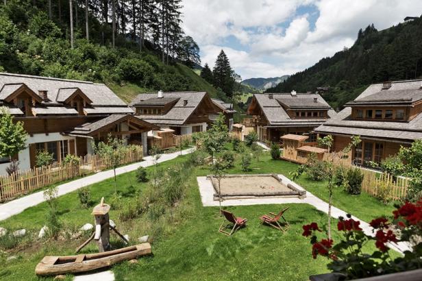 Mehrere Holzhäuser mit Gärten in einer grünen Landschaft.
