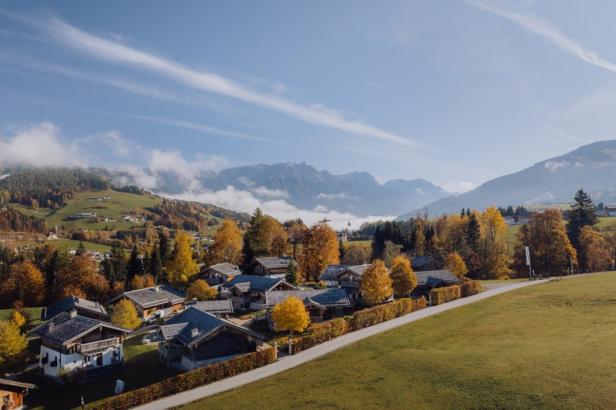Ein Dorf in den Bergen mit herbstlich gefärbten Bäumen unter blauem Himmel.