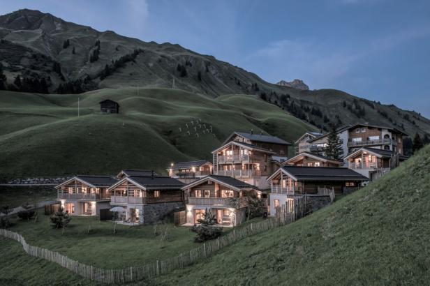 Mehrere Chalets liegen in einer grünen Berglandschaft am Abend.