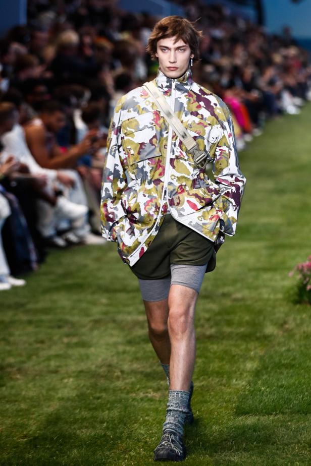 Ein Mann in einer gemusterten Jacke läuft über einen Rasen bei einer Modenschau.