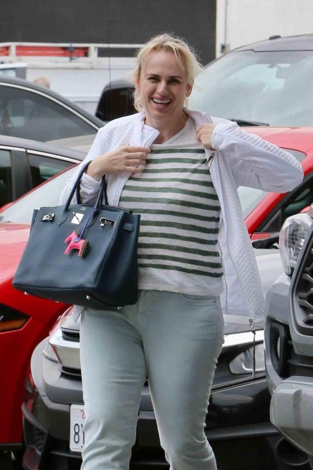 Rebel Wilson lächelt vor geparkten Autos.