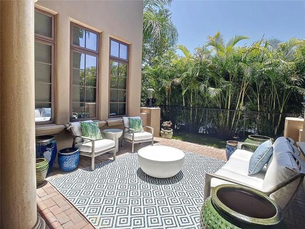 Eine Terrasse mit weißen Möbeln, einem geometrischen Teppich und tropischen Pflanzen im Hintergrund.