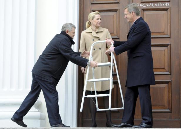 Zwei Männer reichen einer Frau eine weiße Leiter.