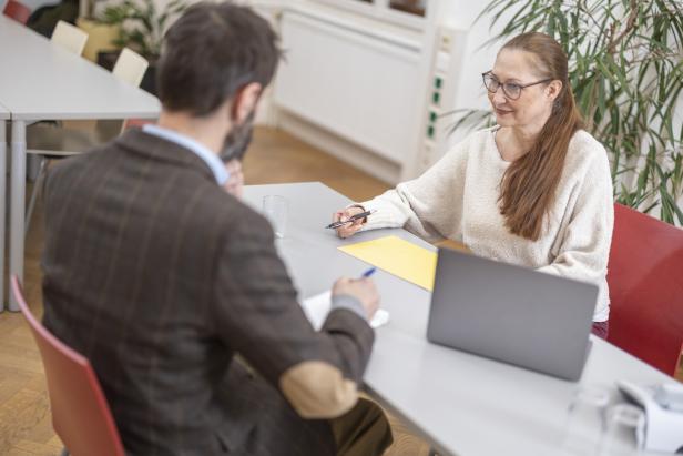 Eine Frau und ein Mann sitzen an einem Tisch mit Laptop und diskutieren.