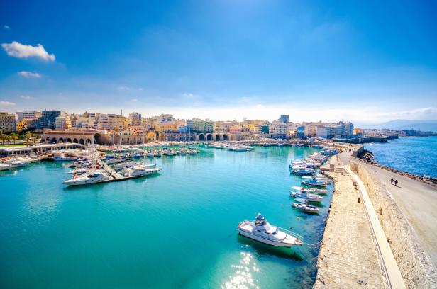 Blick auf den Hafen von Rethymno mit zahlreichen Booten und der Stadt im Hintergrund.