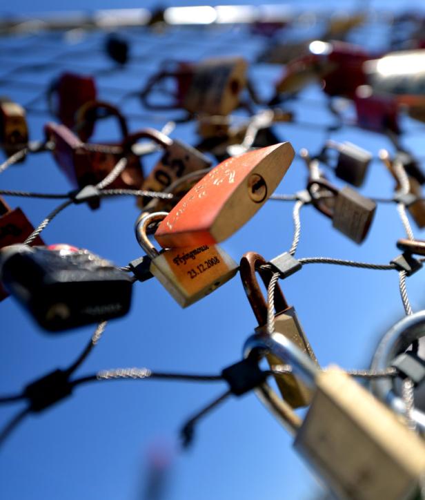 Viele Liebesschlösser hängen an einem Gitter vor blauem Himmel.