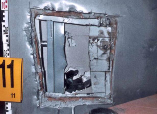 Ein beschädigtes, rechteckiges Loch in einer Wand mit freiliegenden Metallstrukturen.