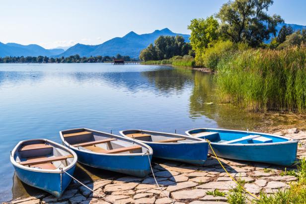 Vier blaue Boote liegen an einem Seeufer mit Blick auf die Berge.