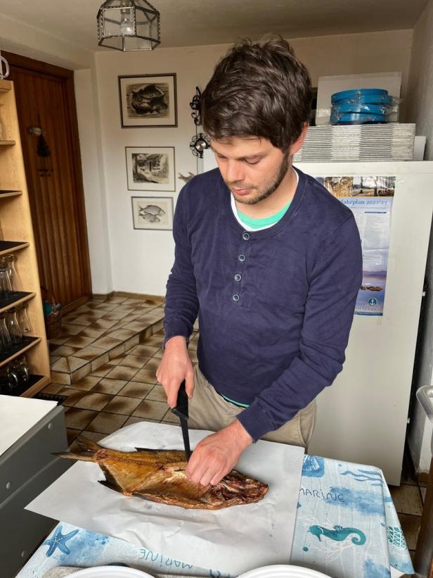 Ein Mann filetiert einen geräucherten Fisch auf einem Tisch.