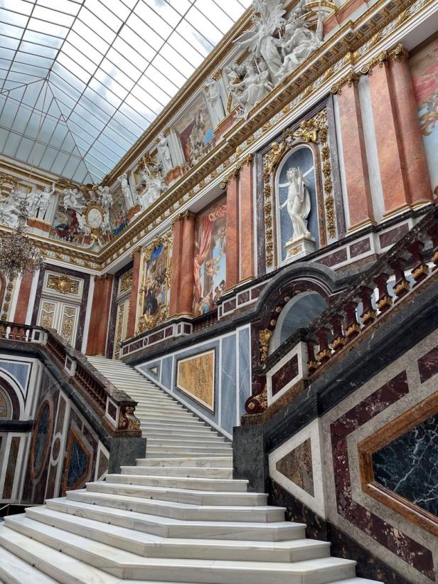 Eine kunstvoll verzierte Treppe in einem prunkvollen Gebäude mit Marmor und Skulpturen.