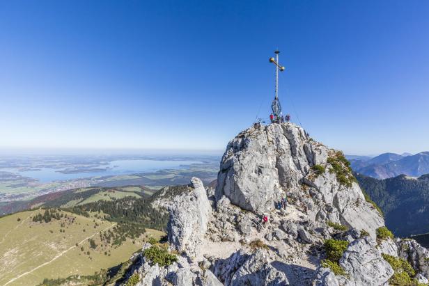 Blick vom Gipfel des felsigen Berges mit Gipfelkreuz auf die Landschaft.