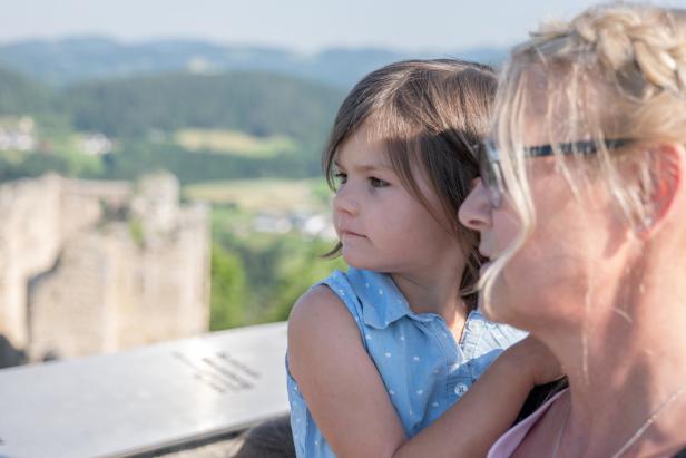 Ein Mädchen und eine Frau schauen auf eine Burgruine in der Ferne.