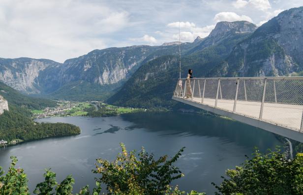 Eine Frau steht auf einer Aussichtsplattform mit Blick auf einen See und Berge.
