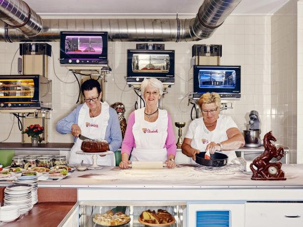 Drei ältere Frauen bereiten in einer Küche Kuchen und Torten zu.
