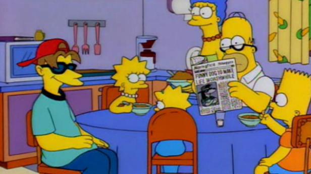 Die Simpsons sitzen am Küchentisch und essen, während Homer Zeitung liest.