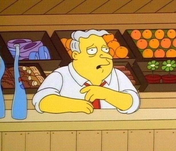 Ein Mann mit grauem Haar steht hinter einer Theke in einem Laden.