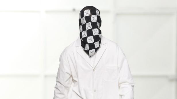 Eine Person mit einem schwarz-weiß gemusterten Tuch über dem Kopf und einem weißen Hemd.