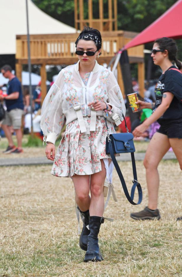 Maisie Williams auf einem Festival in einem geblümten Kleid und schwarzen Stiefeln.