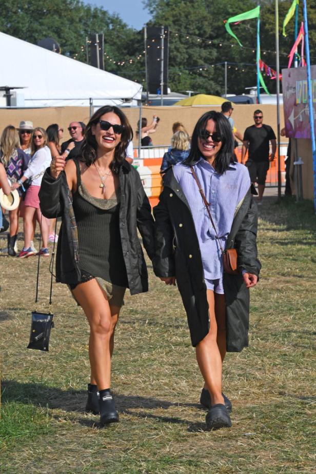 Zwei Frauen mit Sonnenbrillen gehen auf einem Festivalgelände nebeneinander her.