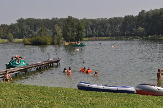 An einem Badesee tummeln sich Menschen im Wasser und auf Tretbooten.
