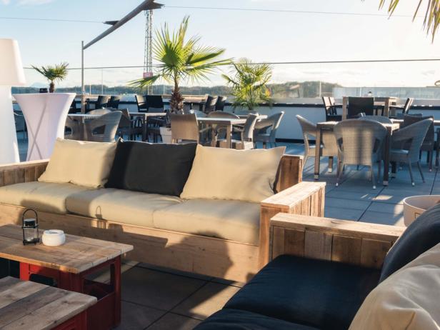 Eine Dachterrasse mit Holzbänken, Tischen und Stühlen lädt zum Verweilen ein.