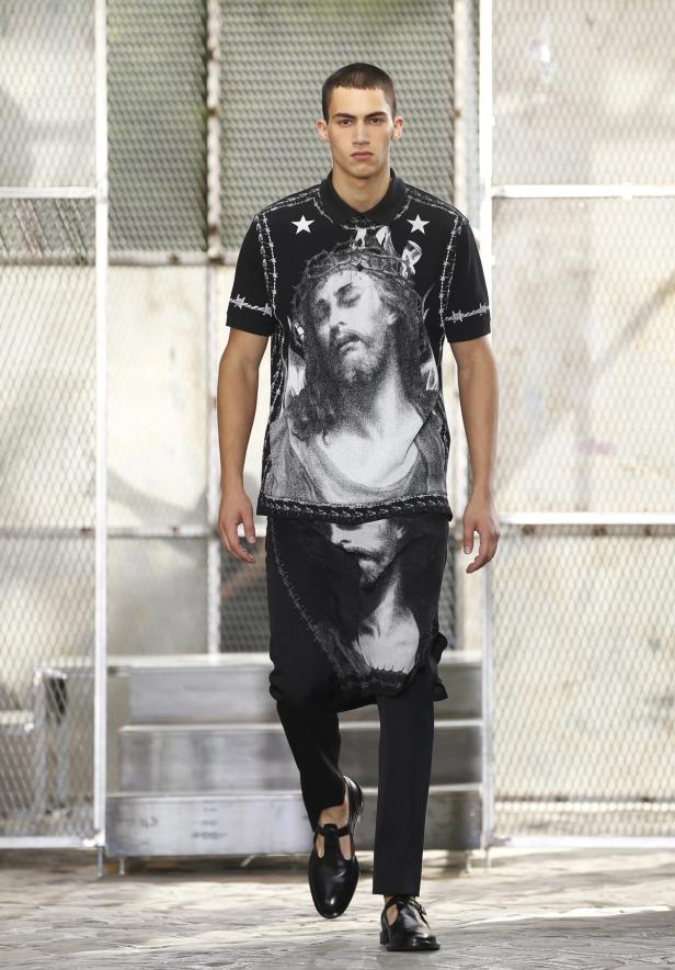 Ein Mann auf einem Laufsteg trägt ein schwarzes Poloshirt mit einem Jesus-Porträt.