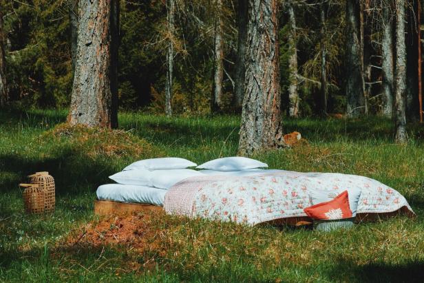 Ein Bett mit Blumenmuster steht auf einer Wiese im Wald.