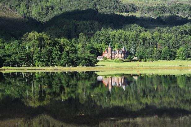 Ein Herrenhaus am See spiegelt sich im ruhigen Wasser.