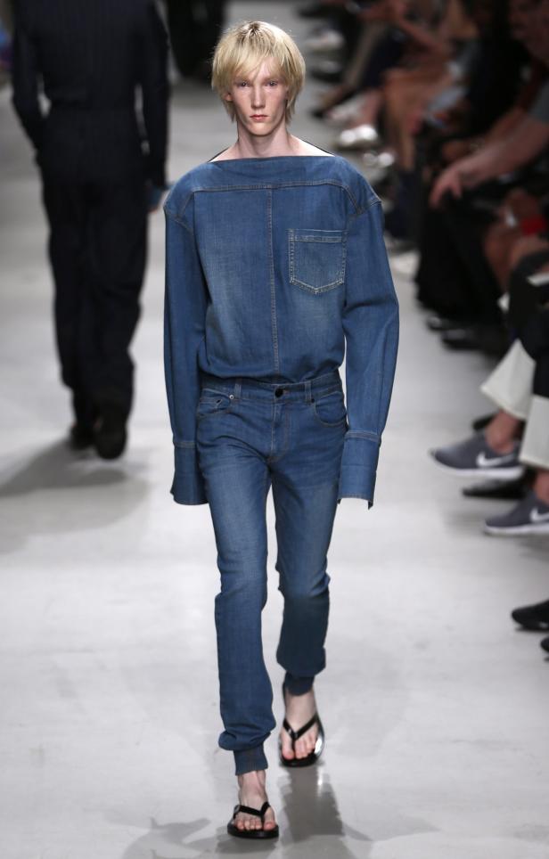 Ein blonder Mann in Jeanshemd und Jeans läuft auf einem Laufsteg.