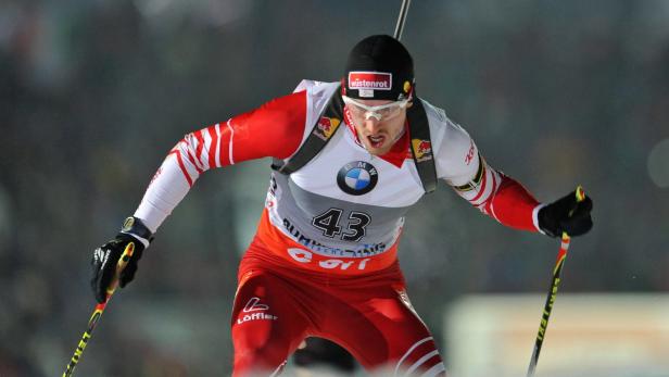 Ein Biathlet in roter und weißer Sportbekleidung beim Skilanglauf.