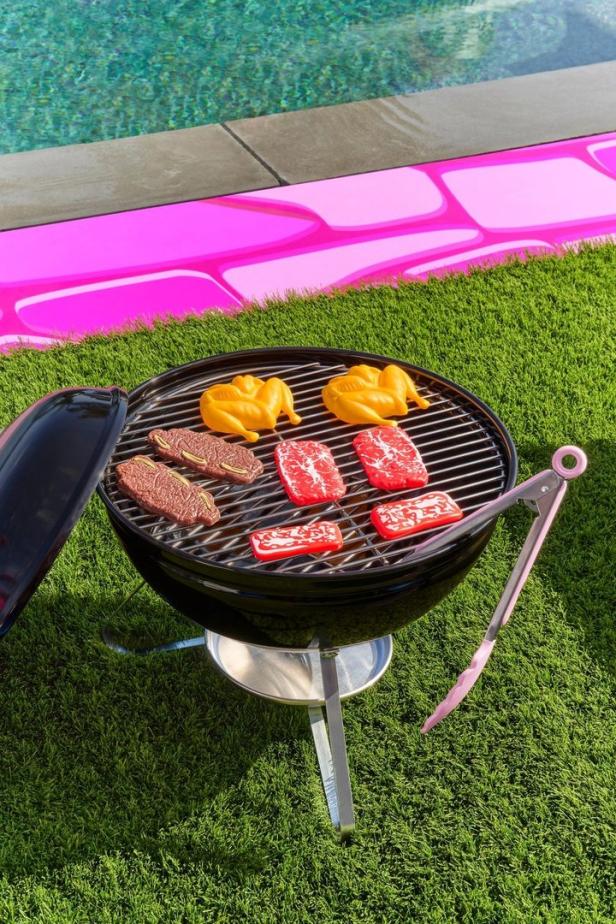 Spielzeug-Grill mit Hähnchen und Fleisch auf einer Wiese neben einem Pool.