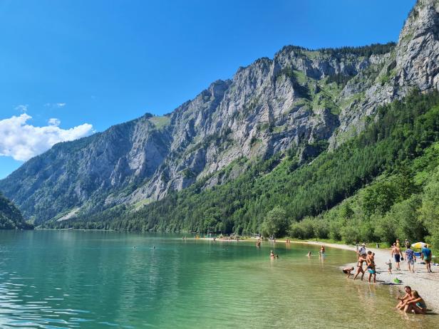 Der smaragdgrüne Traunsee mit Badegästen vor einer steilen Felswand.