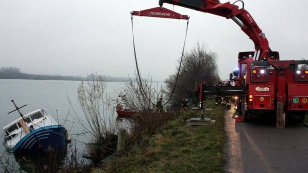 Ein Feuerwehrkran hebt ein gesunkenes Boot aus einem See.