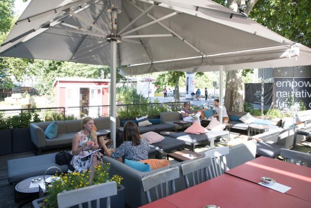 Gäste sitzen auf einer Terrasse unter einem großen Sonnenschirm.