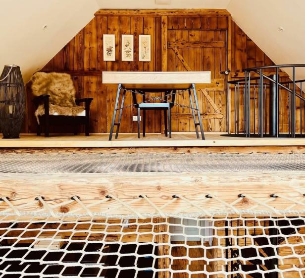 Ein Dachzimmer mit Holzwänden, einem Schreibtisch und einem Netz als Boden.