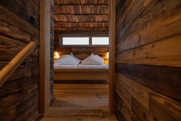 Blick durch eine Holztür auf ein Schlafzimmer mit Holzwänden und einem Doppelbett.