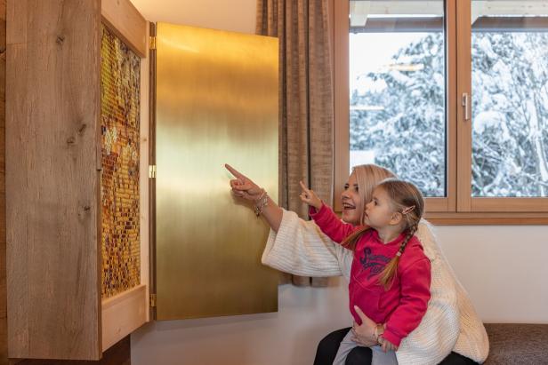 Eine Frau zeigt mit einem kleinen Mädchen auf ein goldenes Element in einem Raum.