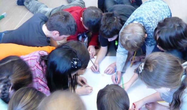 Eine Gruppe Kinder liegt auf dem Boden und malt gemeinsam auf einem großen Blatt Papier.