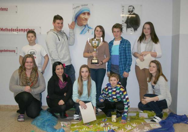 Eine Gruppe von Schülern posiert mit einem Pokal vor Postern von Mutter Teresa und Henry Dunant.