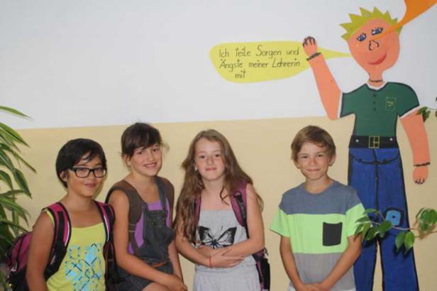Vier Kinder stehen vor einer Wand mit der Aufschrift „Ich teile Sorgen und Ängste meiner Lehrerin mit“.