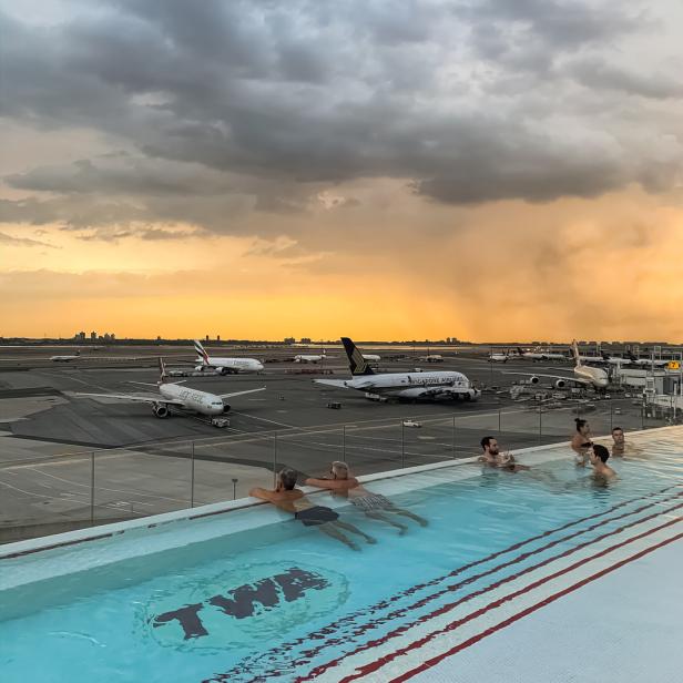 Menschen schwimmen im Pool des TWA Hotels mit Blick auf den Flughafen JFK bei Sonnenuntergang.
