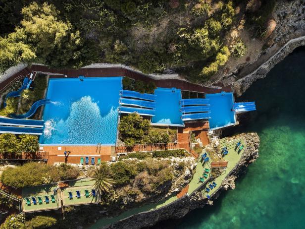Luftaufnahme eines Schwimmbadkomplexes am Meer mit Rutschen und Liegestühlen.